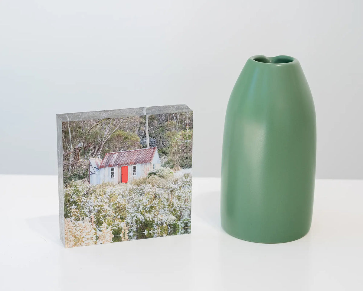 Stockmans Shelter. Acrylic block of Horse Camp Hut, Kosciuszko National Park, styled on a shelf with small vase.