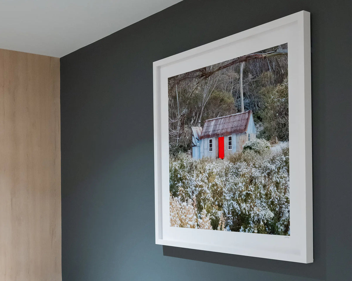 Stockman's Shelter. Horse Camp Hut with snow, Kosciuszko National Park, with white frame hung on charcoal grey wall. 