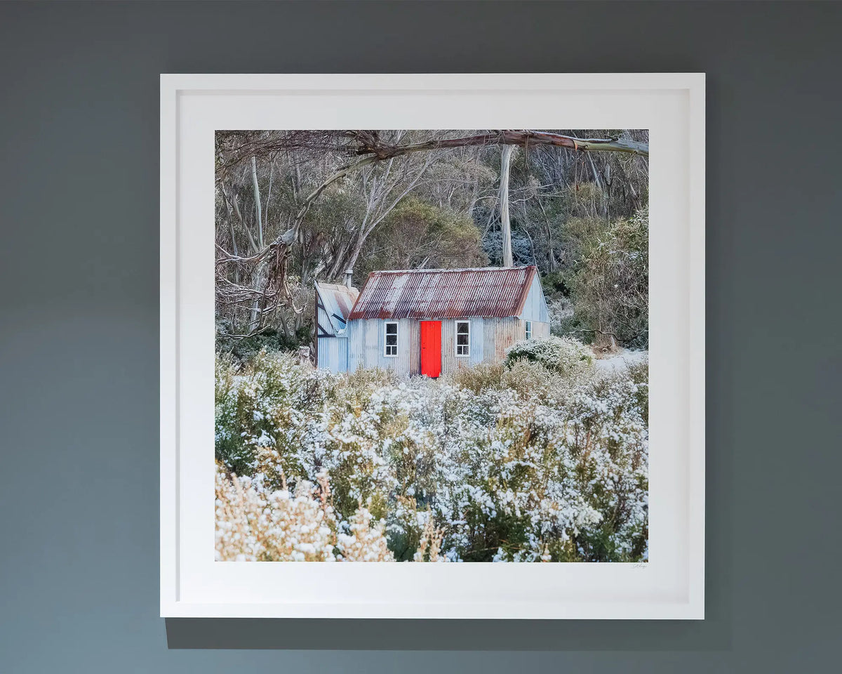 Stockman's Shelter. Horse Camp Hut with snow, Kosciuszko National Park, with white frame hung on dark grey wall. 