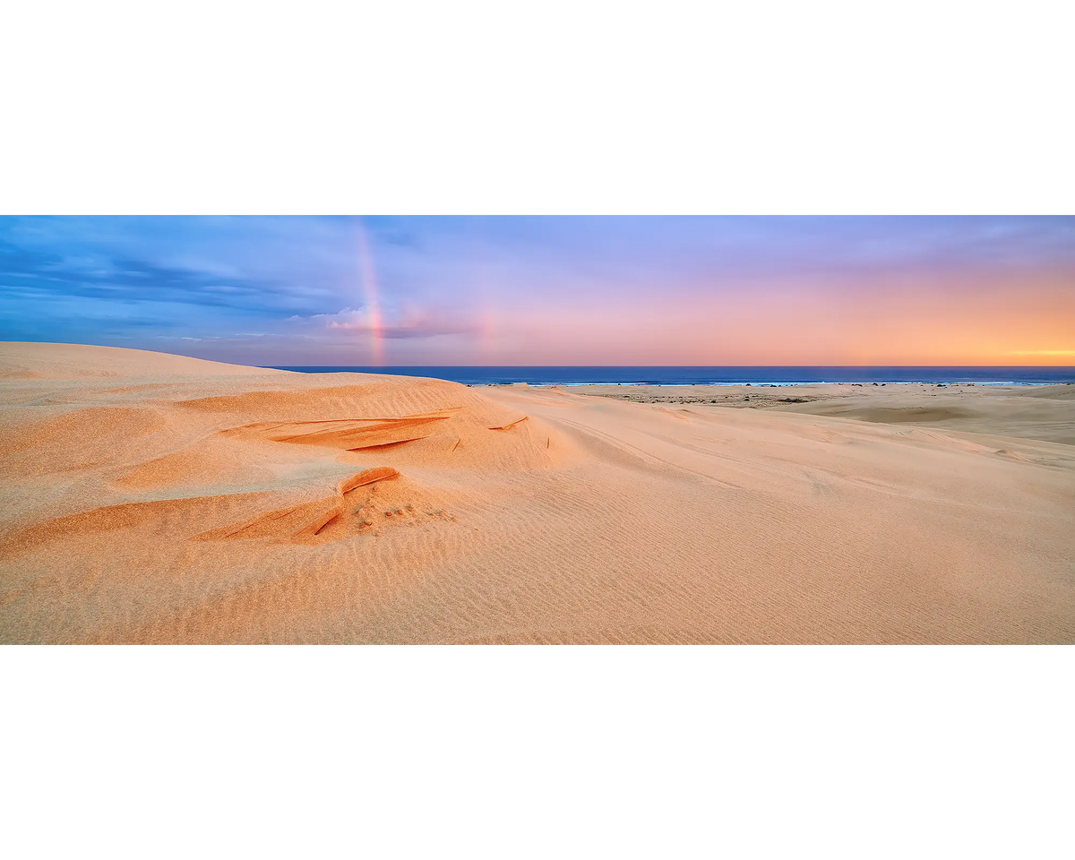 Stockton sand dunes and a rainbow in the sky at sunset.