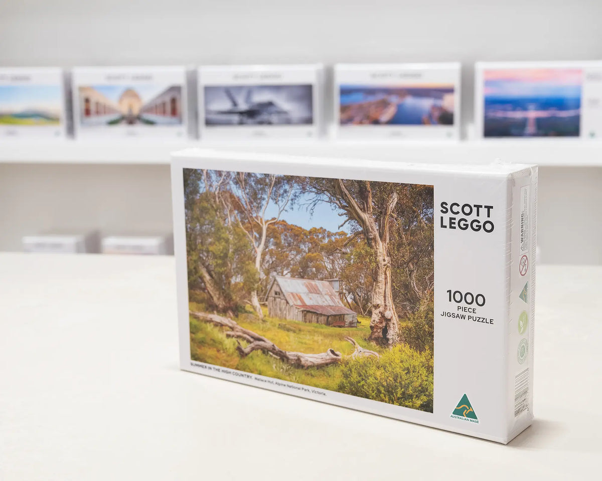 Summer In The High Country 1000 piece Wallace Hut jigsaw puzzle, sitting on table in front of other puzzle boxes.