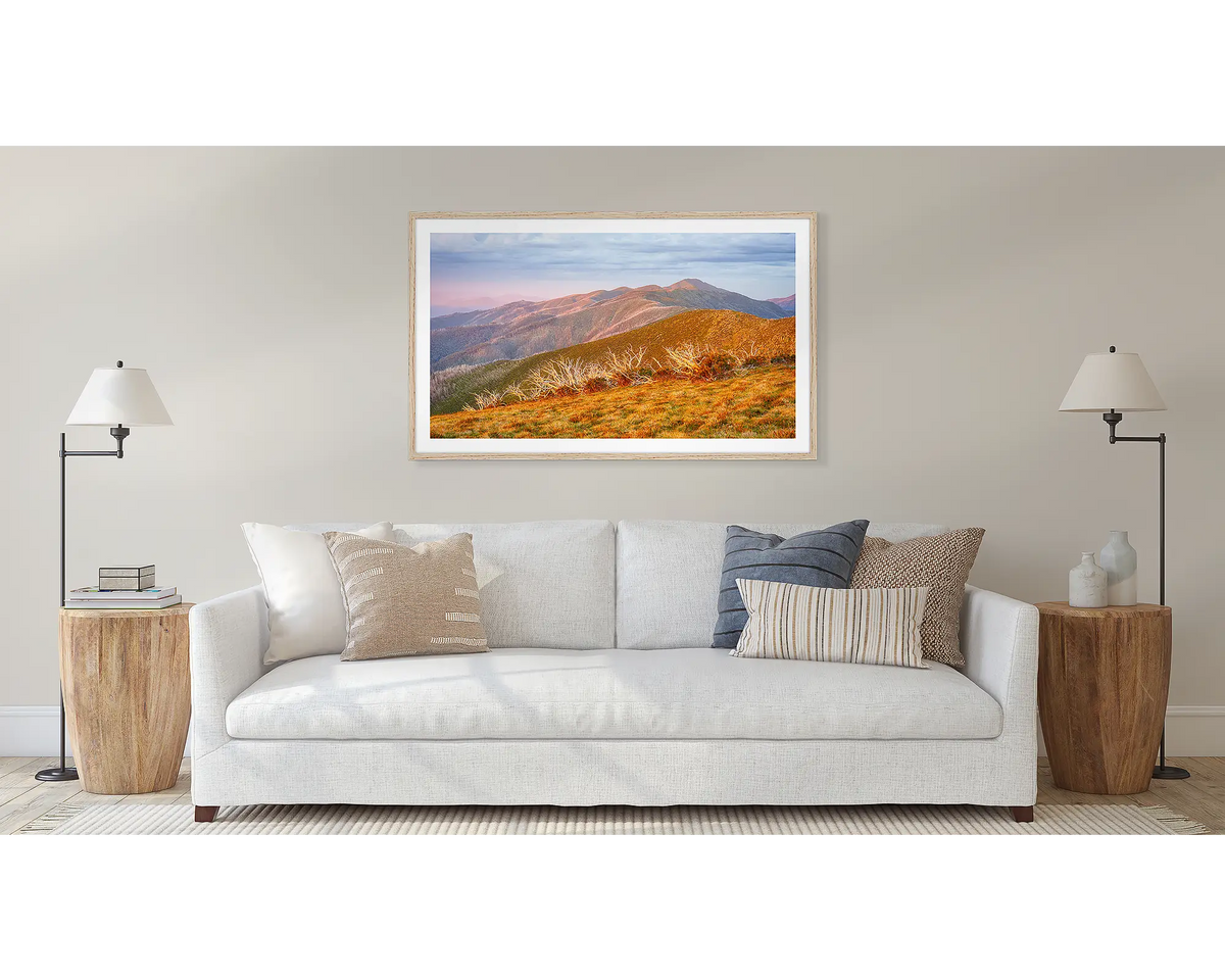 Summer Light framed landscape art print with a timber frame, hung on a beige wall above a white sofa in a modern living room setting.