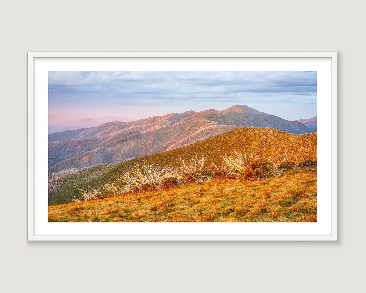 A framed landscape art print depicting sunset over Mount Feathertop, presented in a white frame against a light grey background.