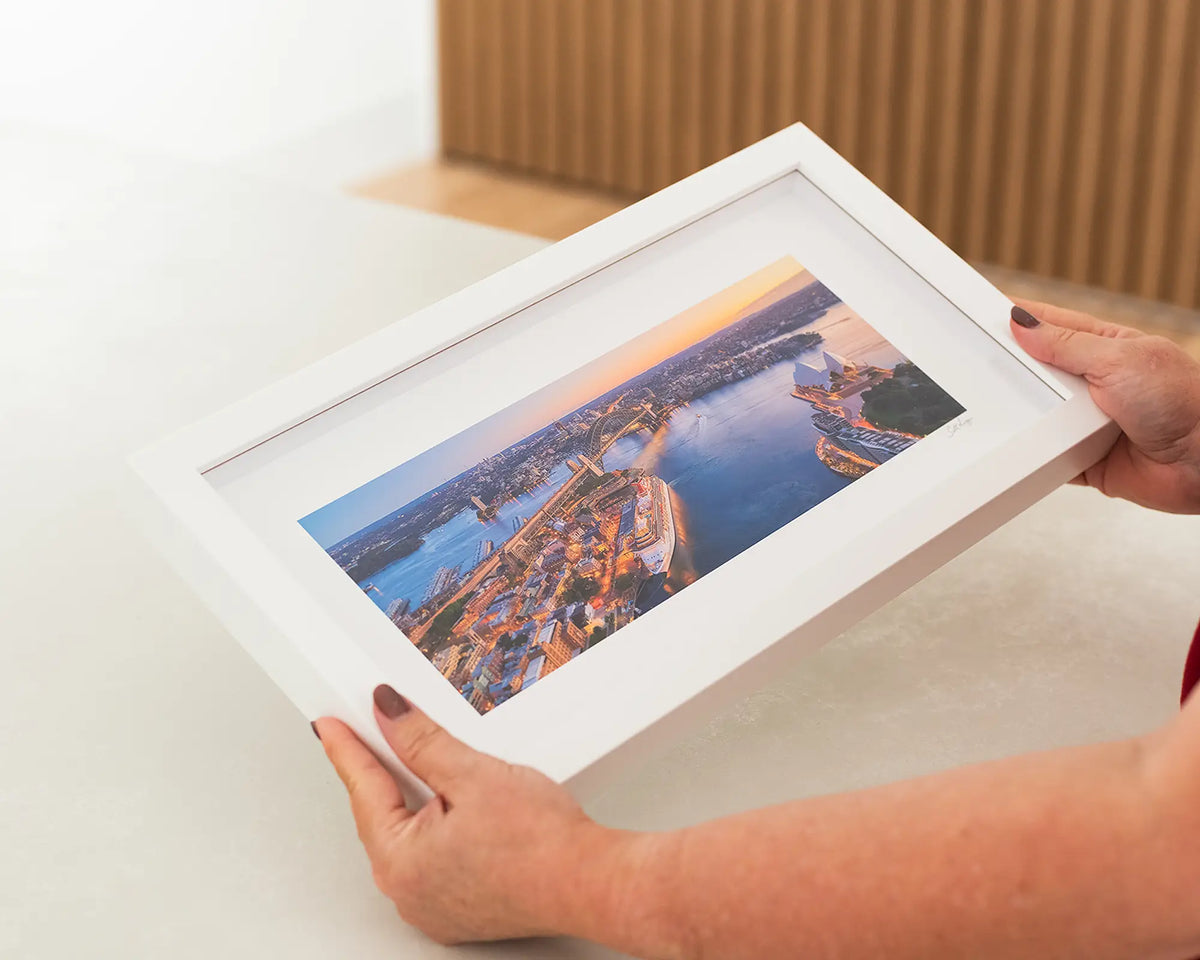 Sydney Awakes. Sunrise over Sydney small frame wall art print with white frame being held.