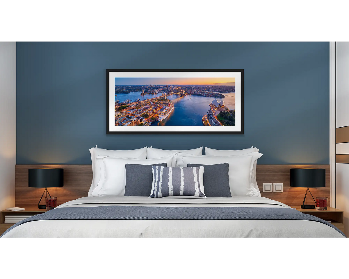 Sydney Awakes. Wall art print of a sunrise over Sydney, framed with a black frame and hung above a bed in a hotel room. 