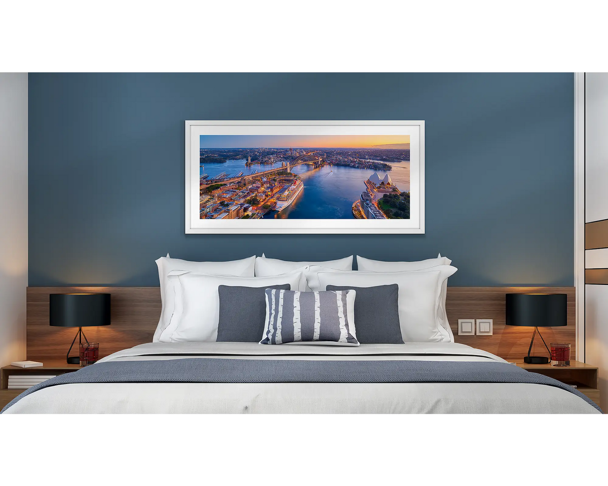Sydney Awakes. Wall art print of a sunrise over Sydney, framed with a white frame and hung above a bed in a hotel room. 