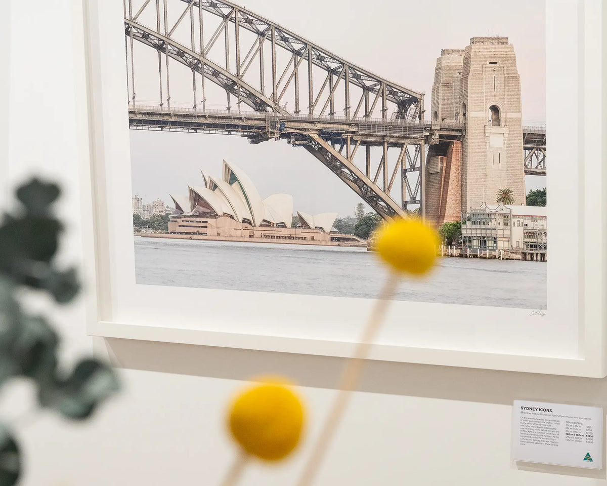 Sydney Icons. Harbour Bridge and Opera House framed wall art hanging in gallery with flowers in foreground.
