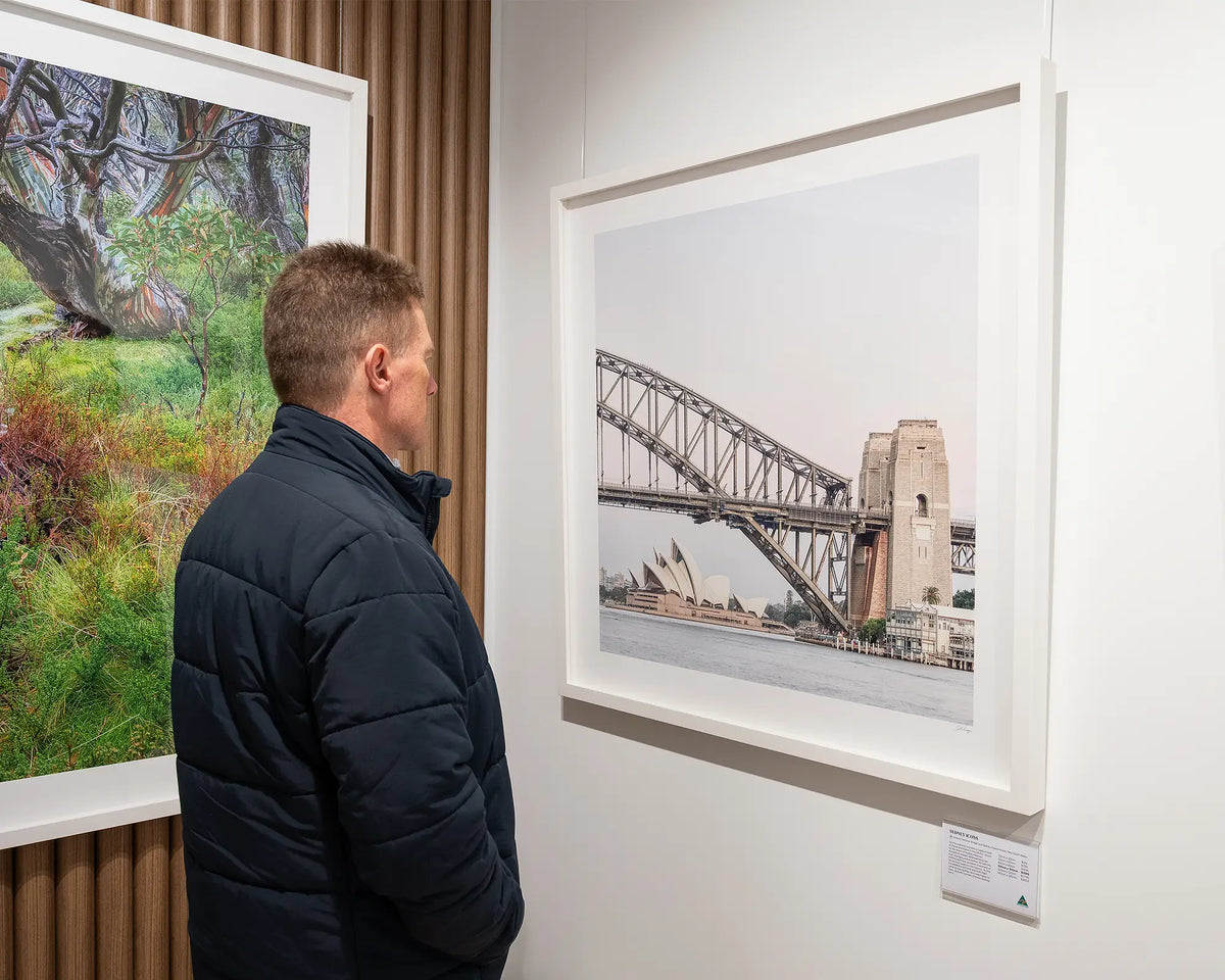 Sydney Icons. Harbour Bridge and Opera House with white frame, on gallery wall with person admiring.