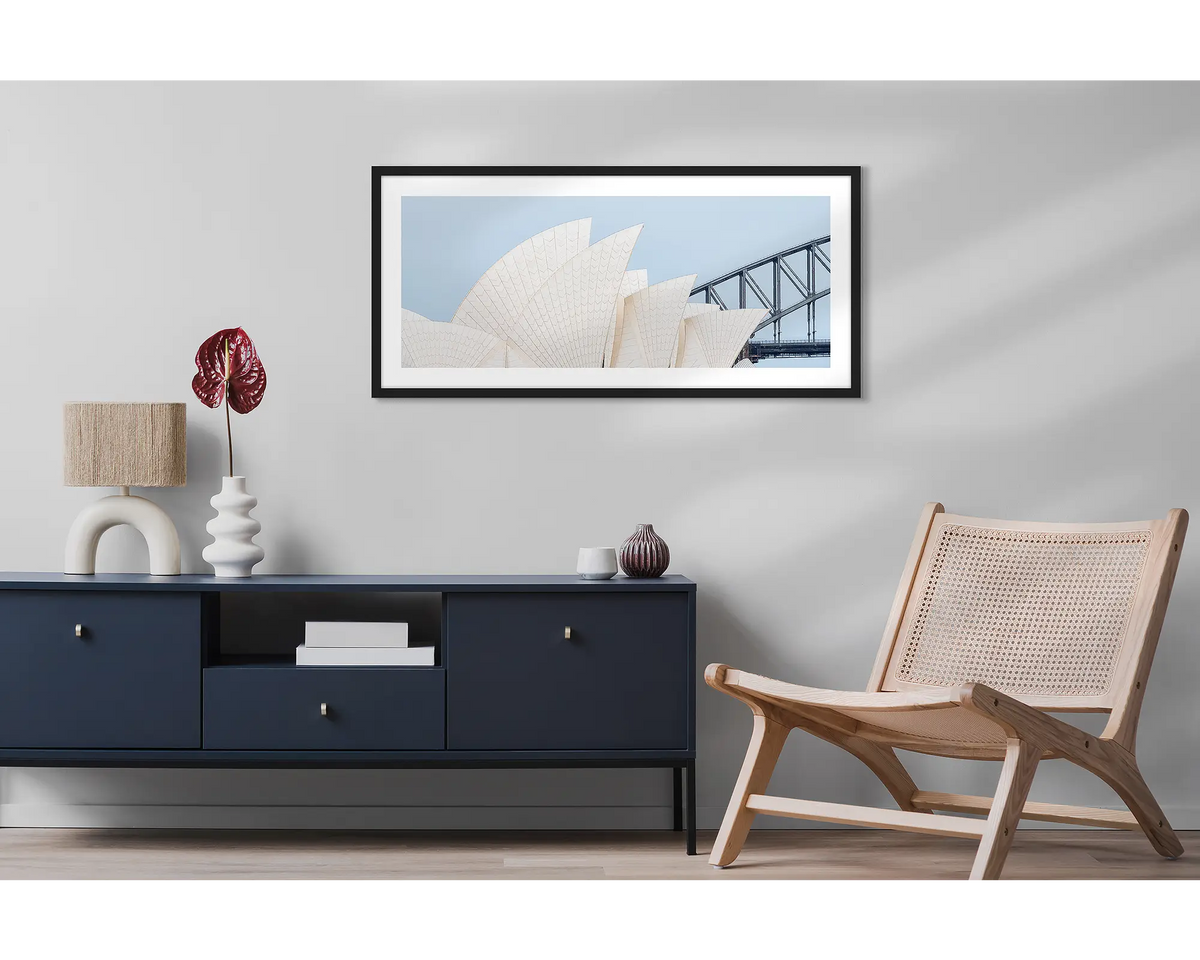 Sydney Outlines. Wall art print featuring Sydney Opera House and Harbour Bridge with a black frame, hung above a side table and chair. 