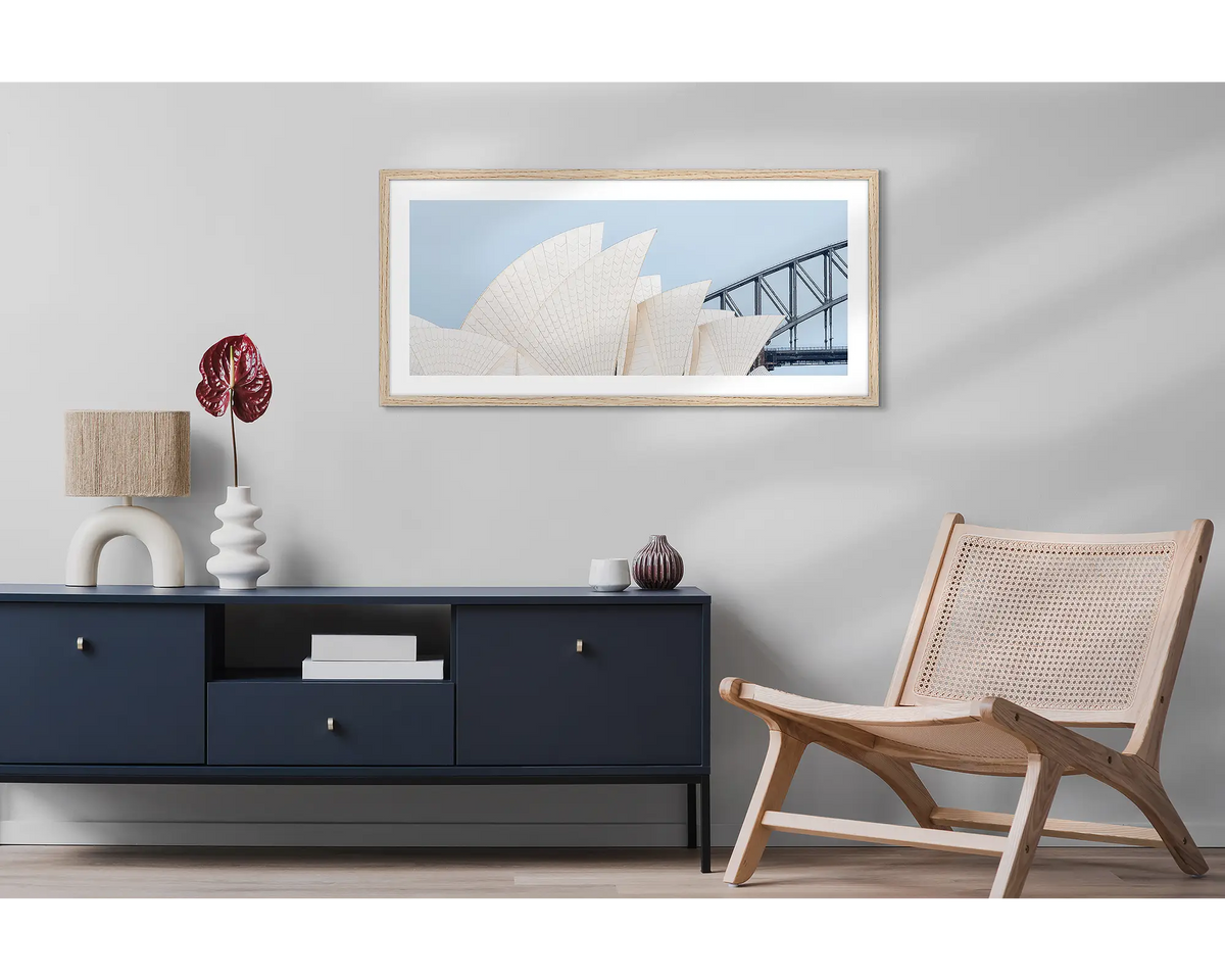 Sydney Outlines. Wall art print featuring Sydney Opera House and Harbour Bridge with a timber frame, hung above a side table and chair. 