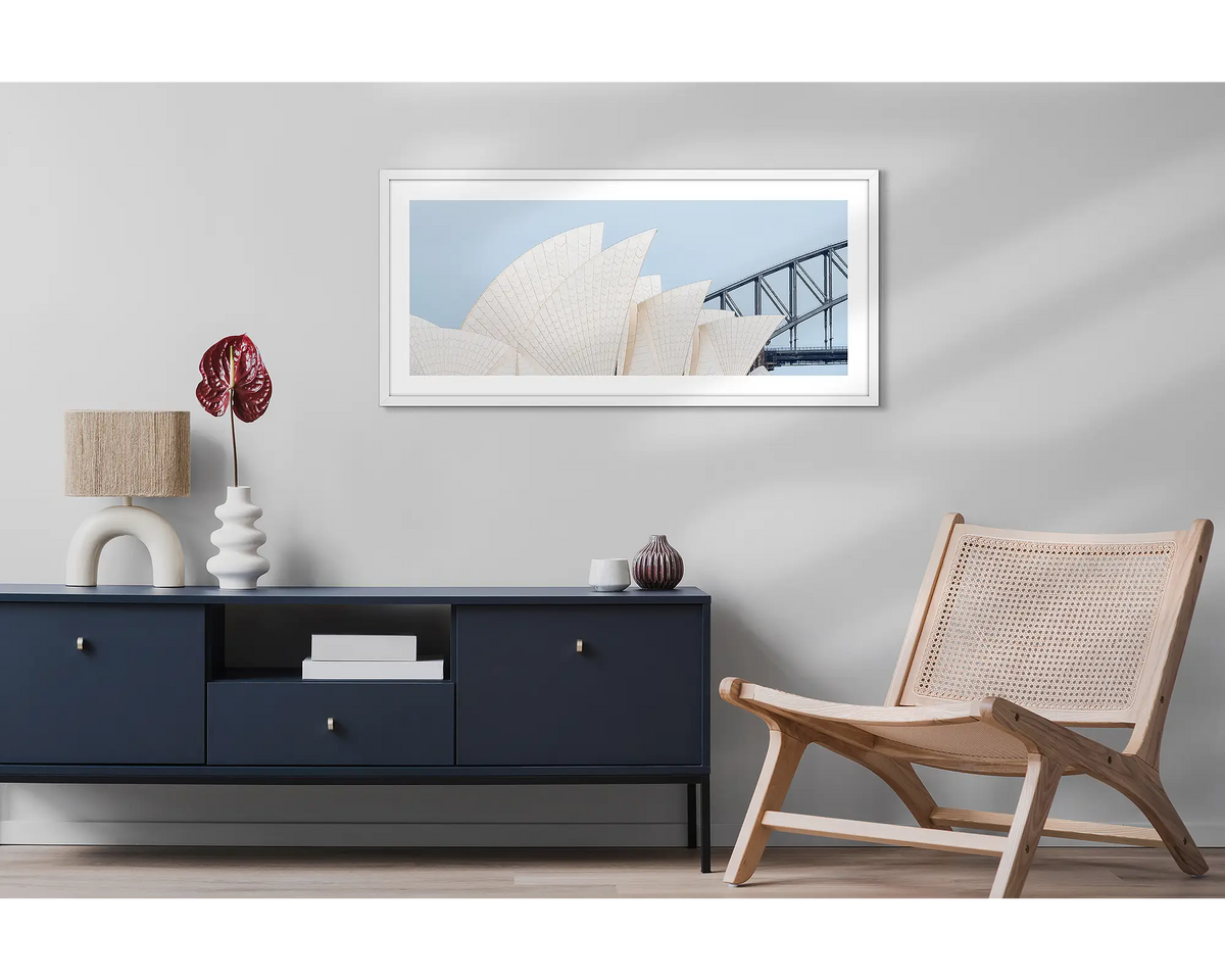 Sydney Outlines. Wall art print featuring Sydney Opera House and Harbour Bridge with a white frame, hung above a side table and chair. 