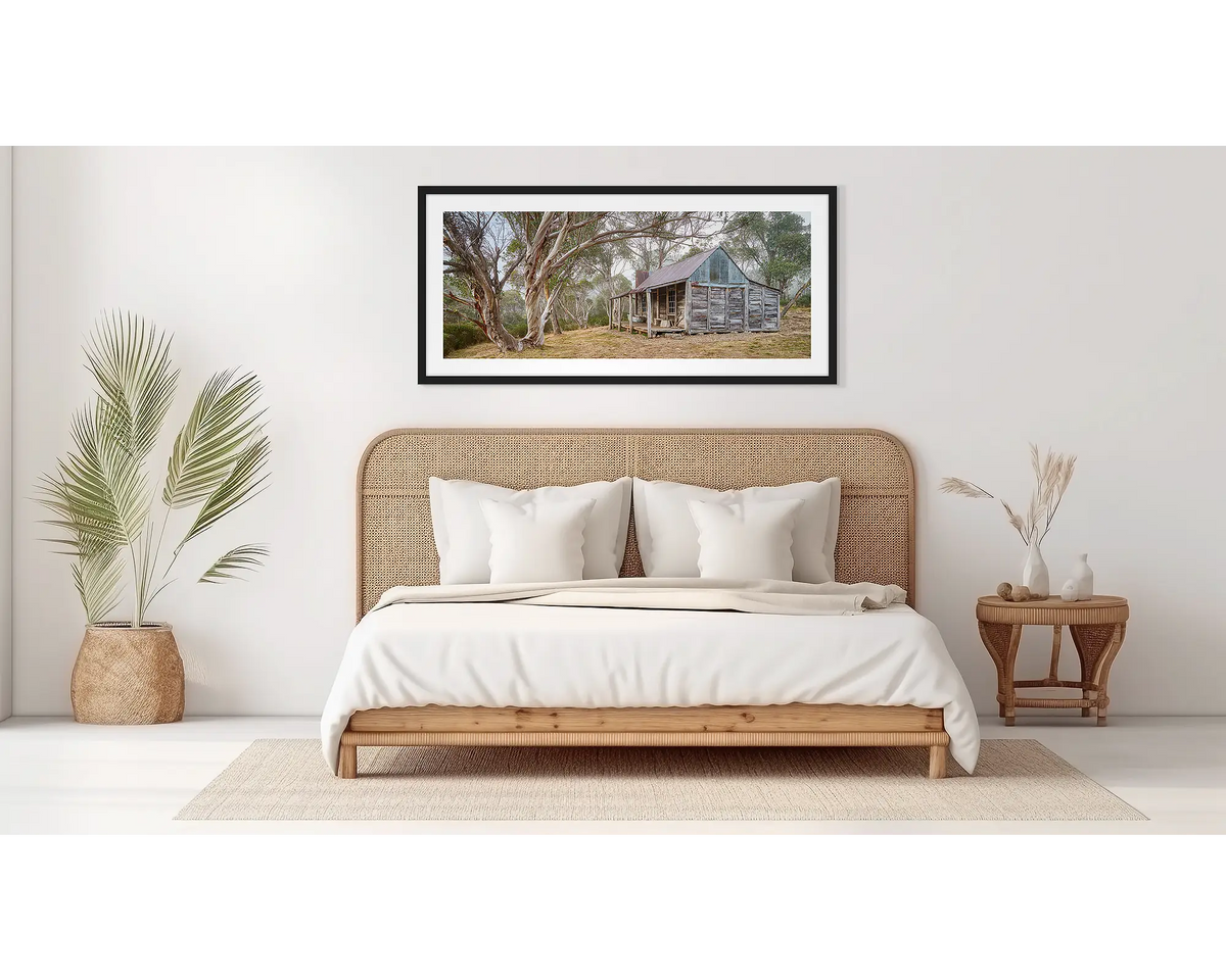 Tales of the Stockman. Wall art print of Wheelers Hut in Kosciuszko National Park with a black frame hung above a bed. 