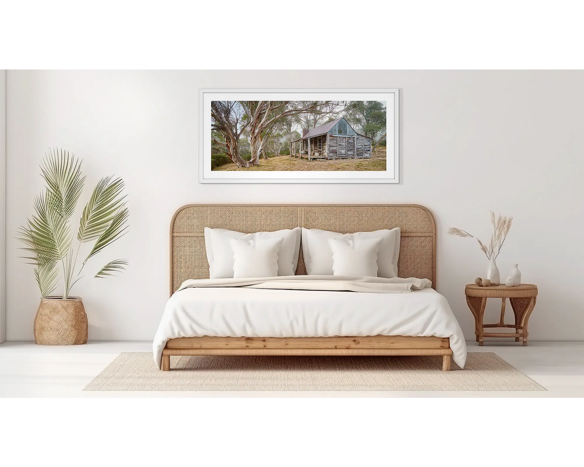 Tales of the Stockman. Wall art print of Wheelers Hut in Kosciuszko National Park with a white frame hung above a bed. 