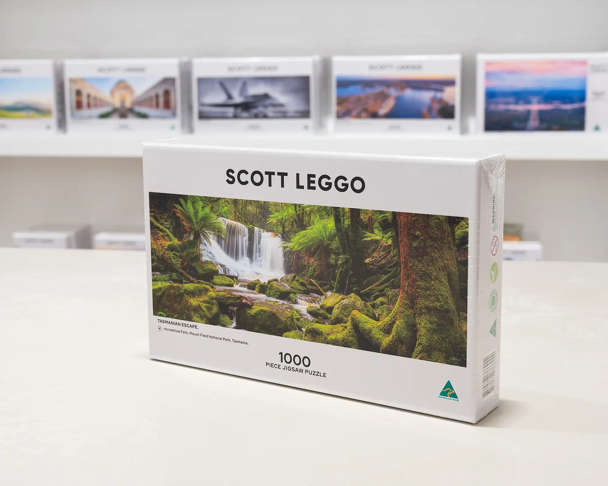 Tasmanian Escape 1000 piece jigsaw puzzle box sitting on table in front of other puzzle boxes.