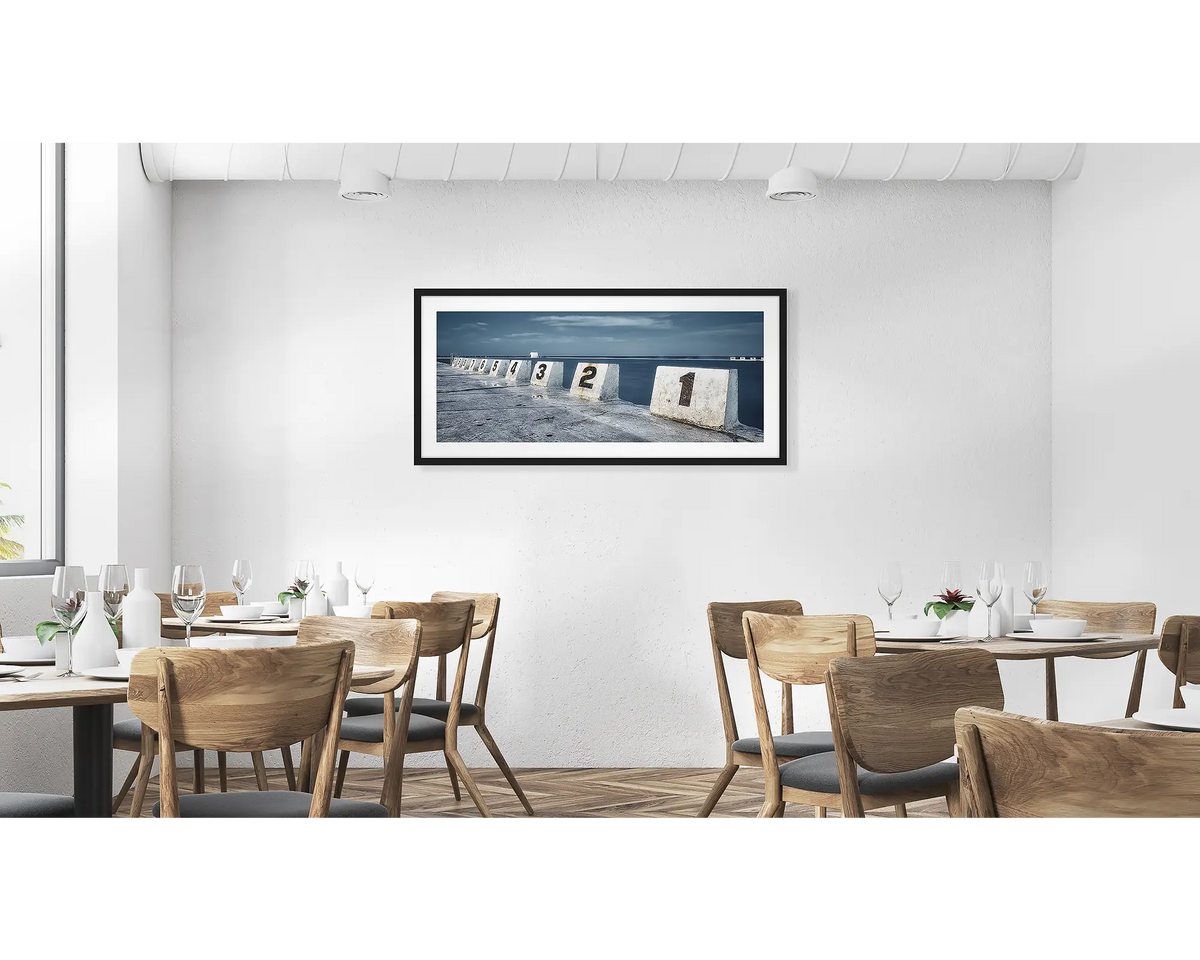 Ten. Merewether ocean baths wall art in a  black frame hung in a cafe. 