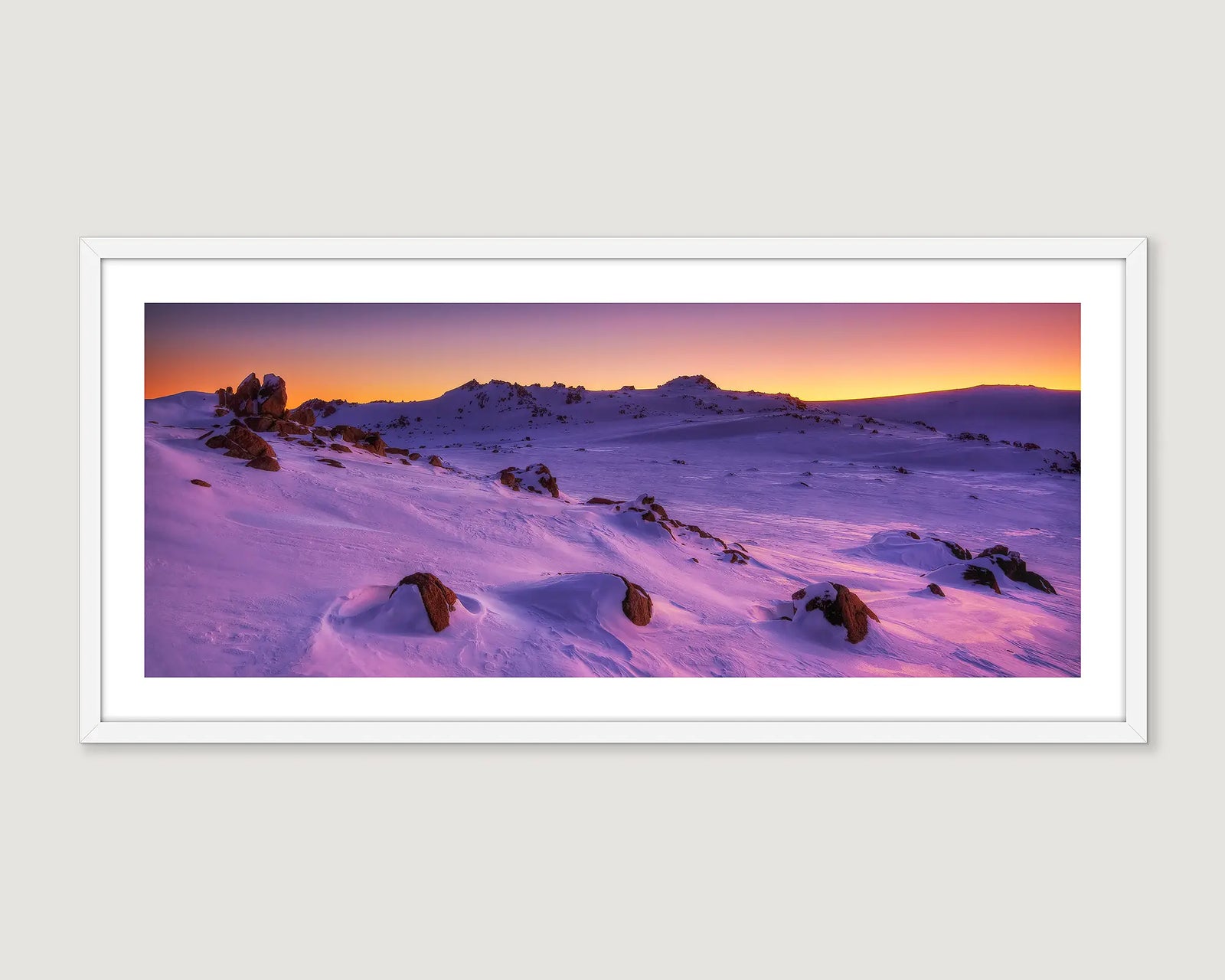 Framed photograph of snow covered mountains at sunset.