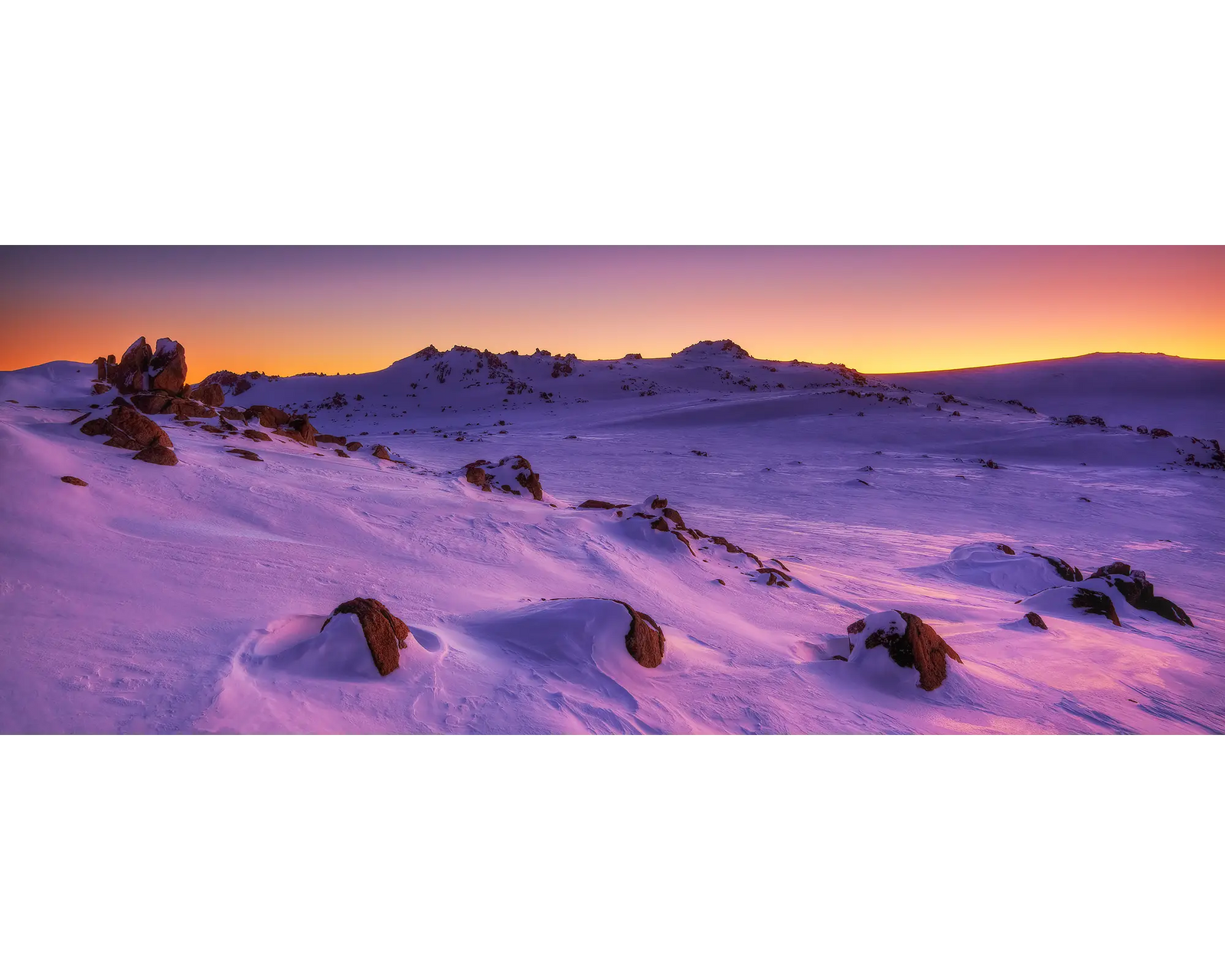 Framed photograph of snow covered mountains at sunset.