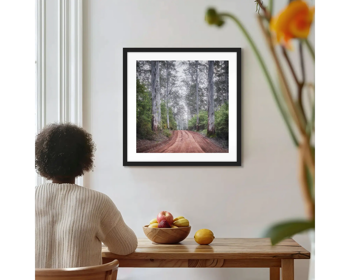 The Forest Beyond. Forest photographic wall art print with a black frame, hung on a kitchen wall with a woman admiring. 