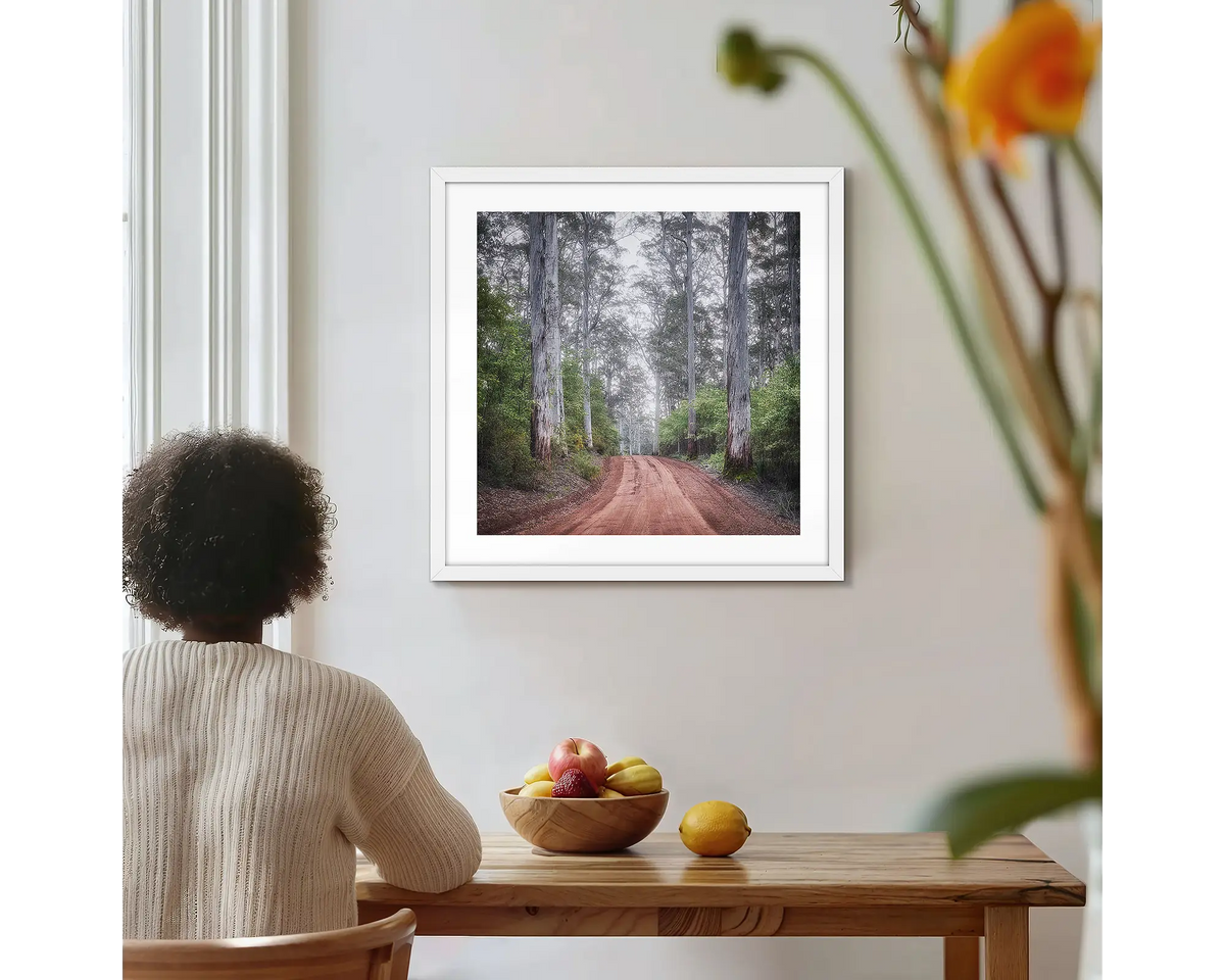 The Forest Beyond. Forest photographic wall art print with a white frame, hung on a kitchen wall with a woman admiring. 