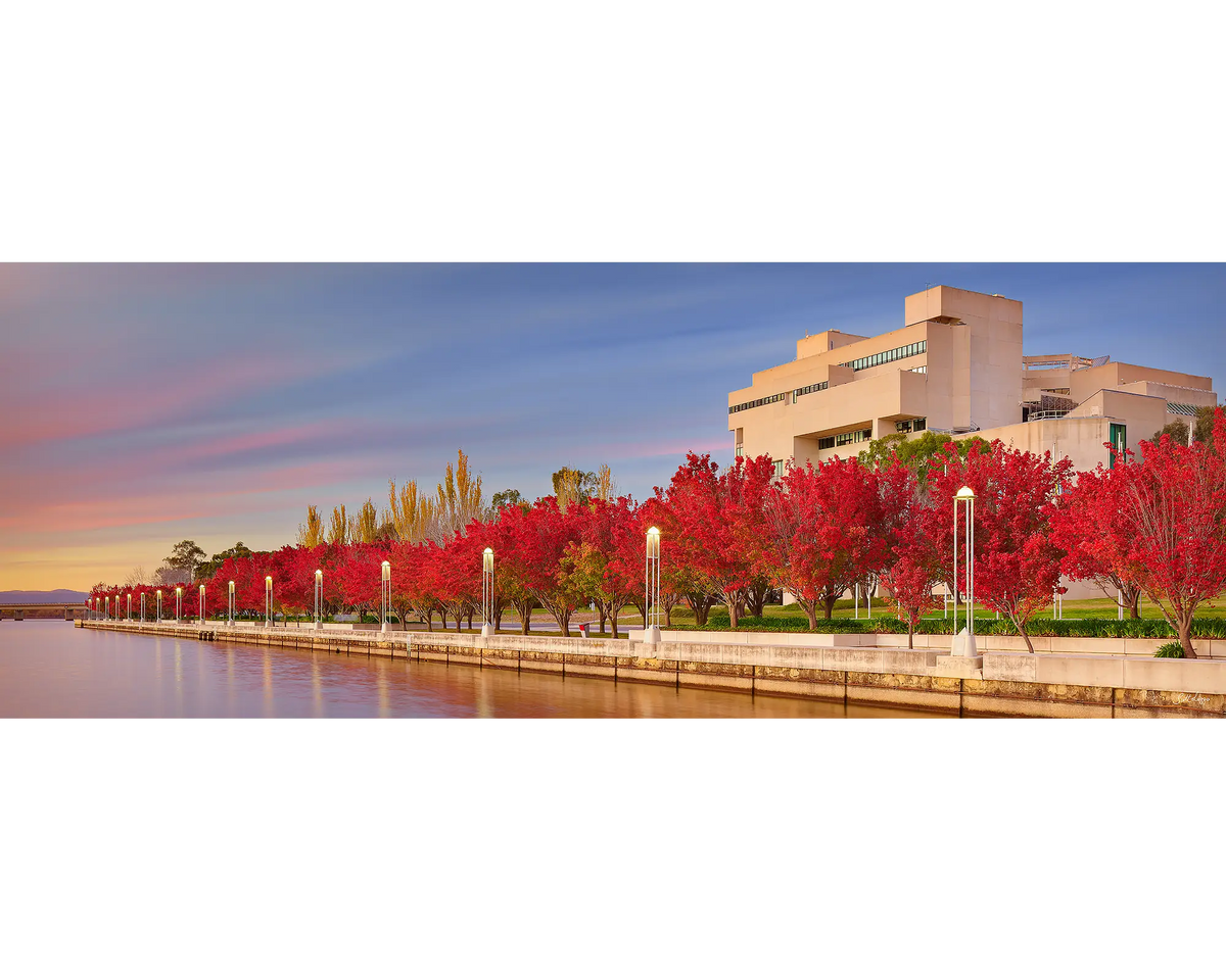 The High Court Of Australia with red autumn trees beside Lake Burley Griffin at sunrise.