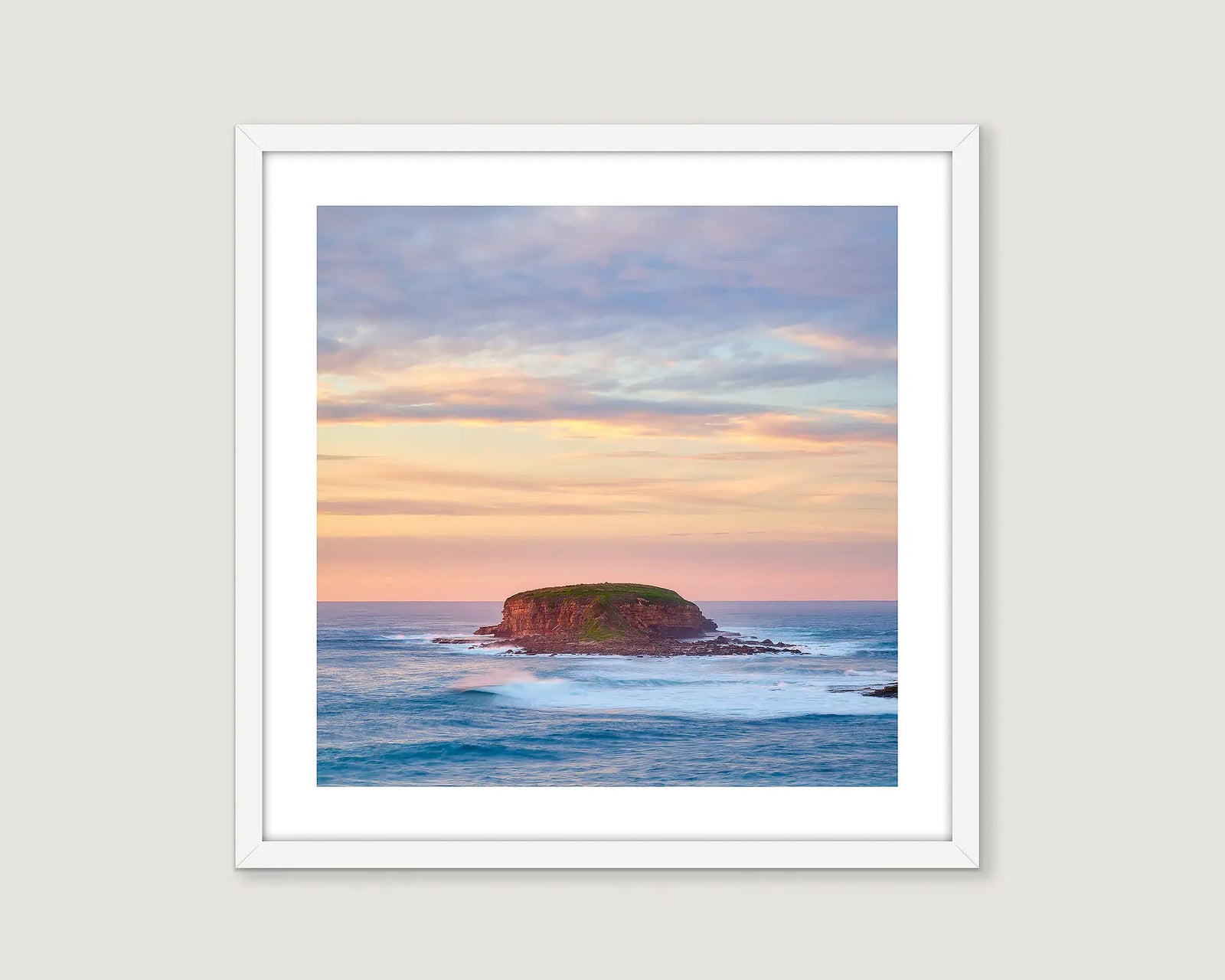 Framed artwork of a coastal scene with a rocky island and colourful sky.