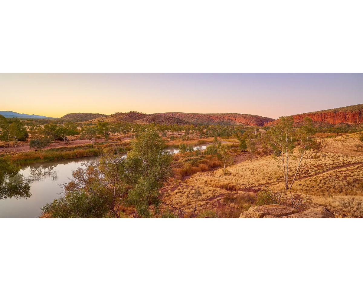 Scenic view of Finke River with red cliffs and gum trees at sunrise.