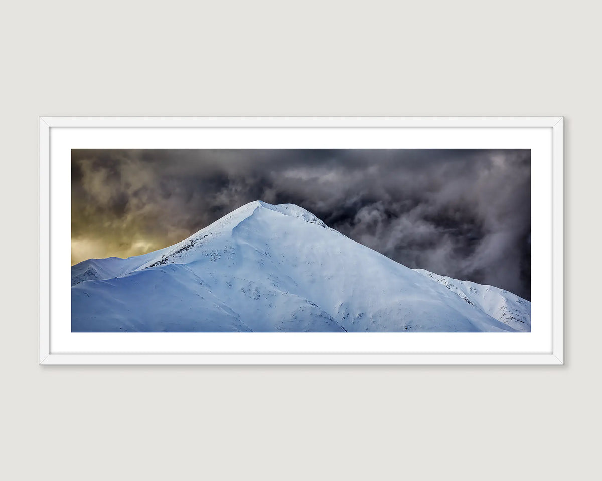 Framed photograph of a snow-covered Mount Feathertop mountain peak with dark clouds above.