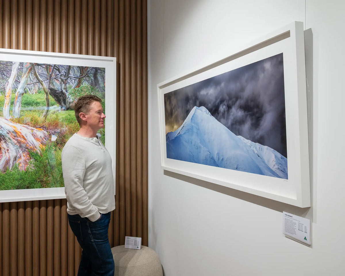 The Summit. Mount Feathertop wall art print with white frame hanging in gallery with person admiring.