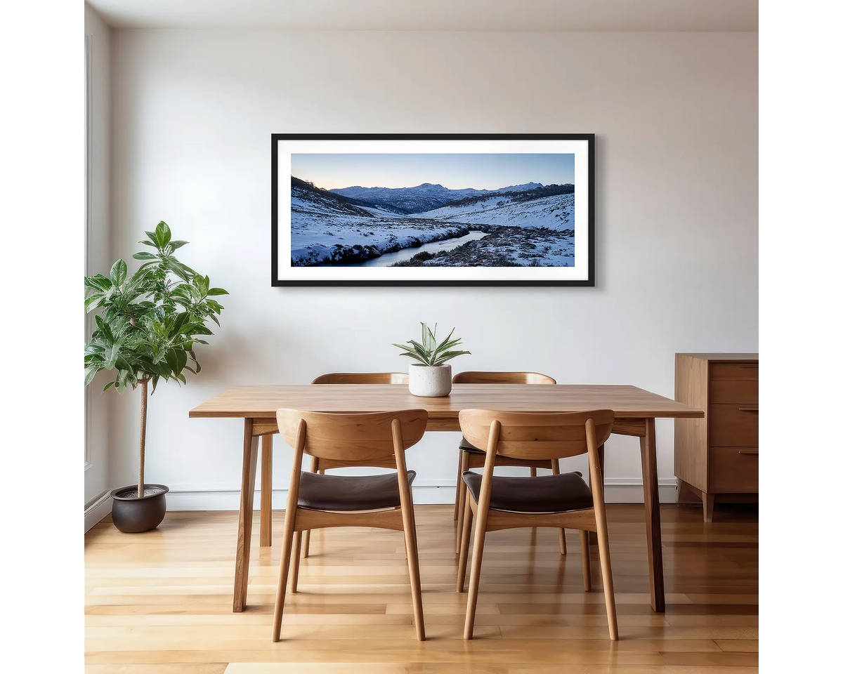Thredbo Colours. Wall art print with a black frame hung in a dining room, featuring the Thredbo River with winter snow.