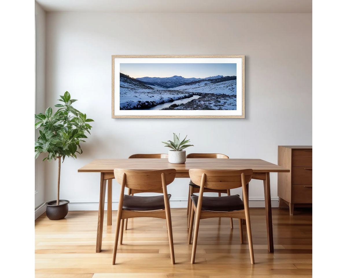 Thredbo Colours. Wall art print with a timber frame hung in a dining room, featuring the Thredbo River with winter snow.