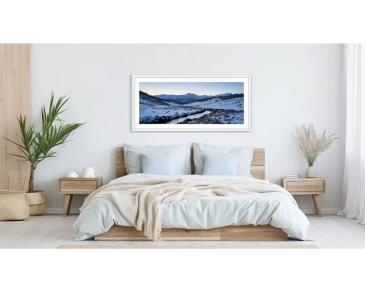 Thredbo Colours. Wall art print with a white frame hung above a bed, featuring the Thredbo River with winter snow.