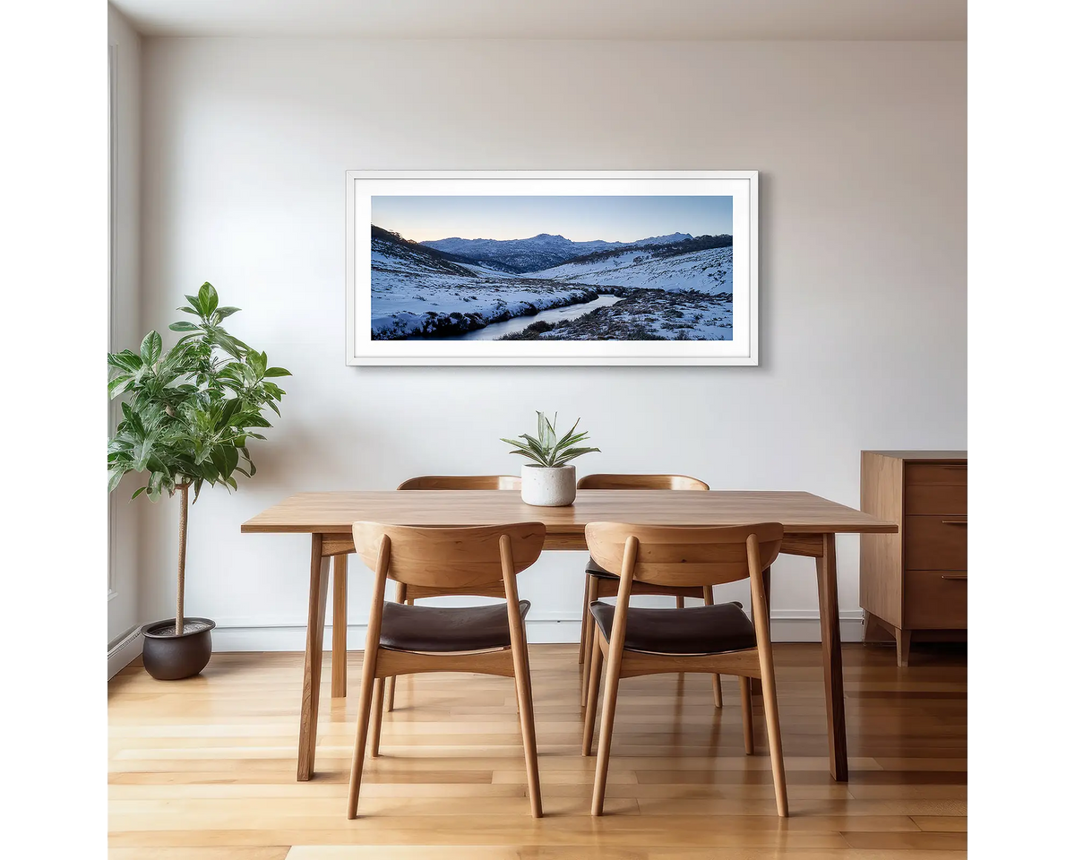 Thredbo Colours. Wall art print with a white frame hung in a dining room, featuring the Thredbo River with winter snow.
