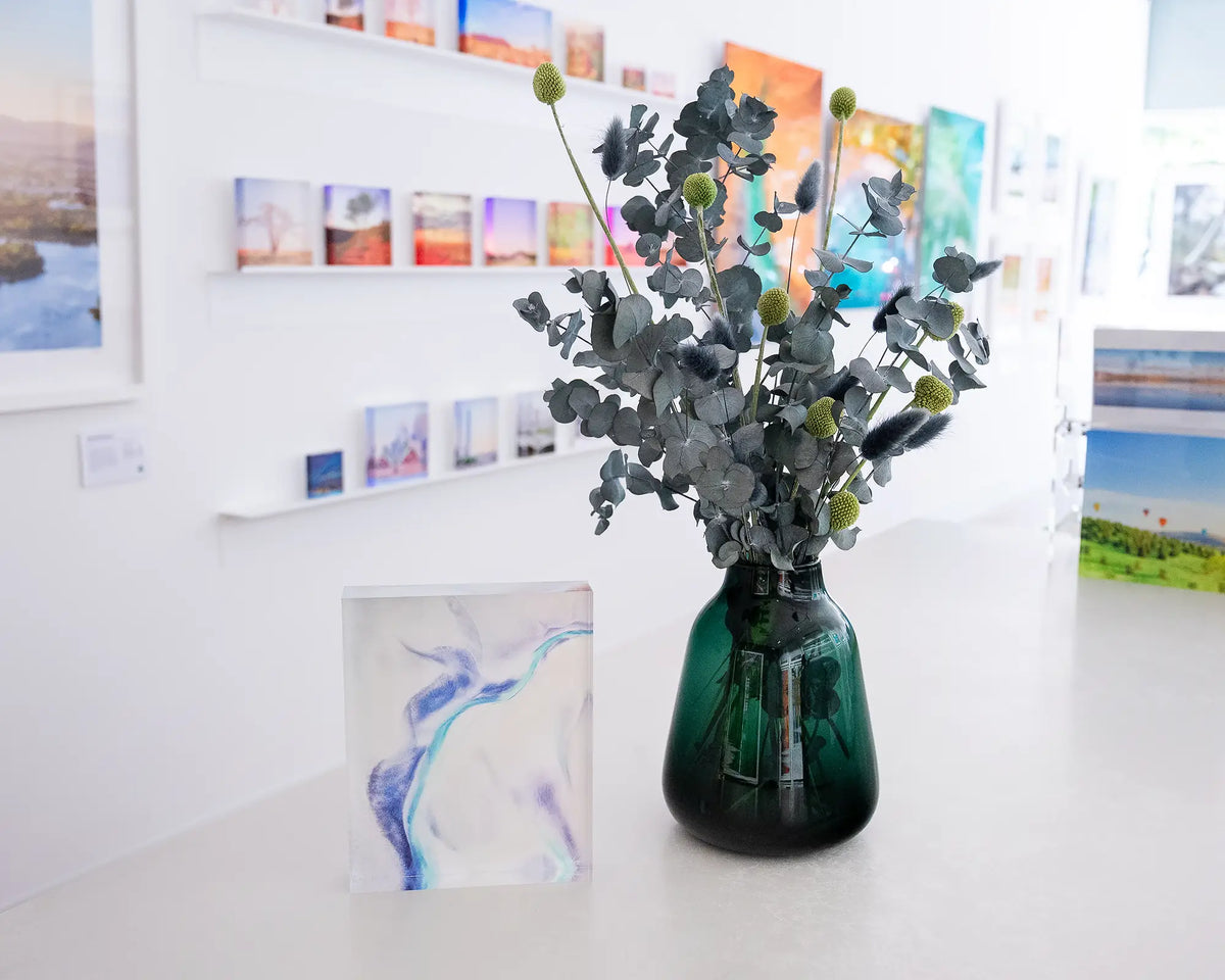 Tidal Orchid. Acrylic block abstract aerial artwork Roebuck Bay, Western Australia, on gallery desk with flower arrangement.