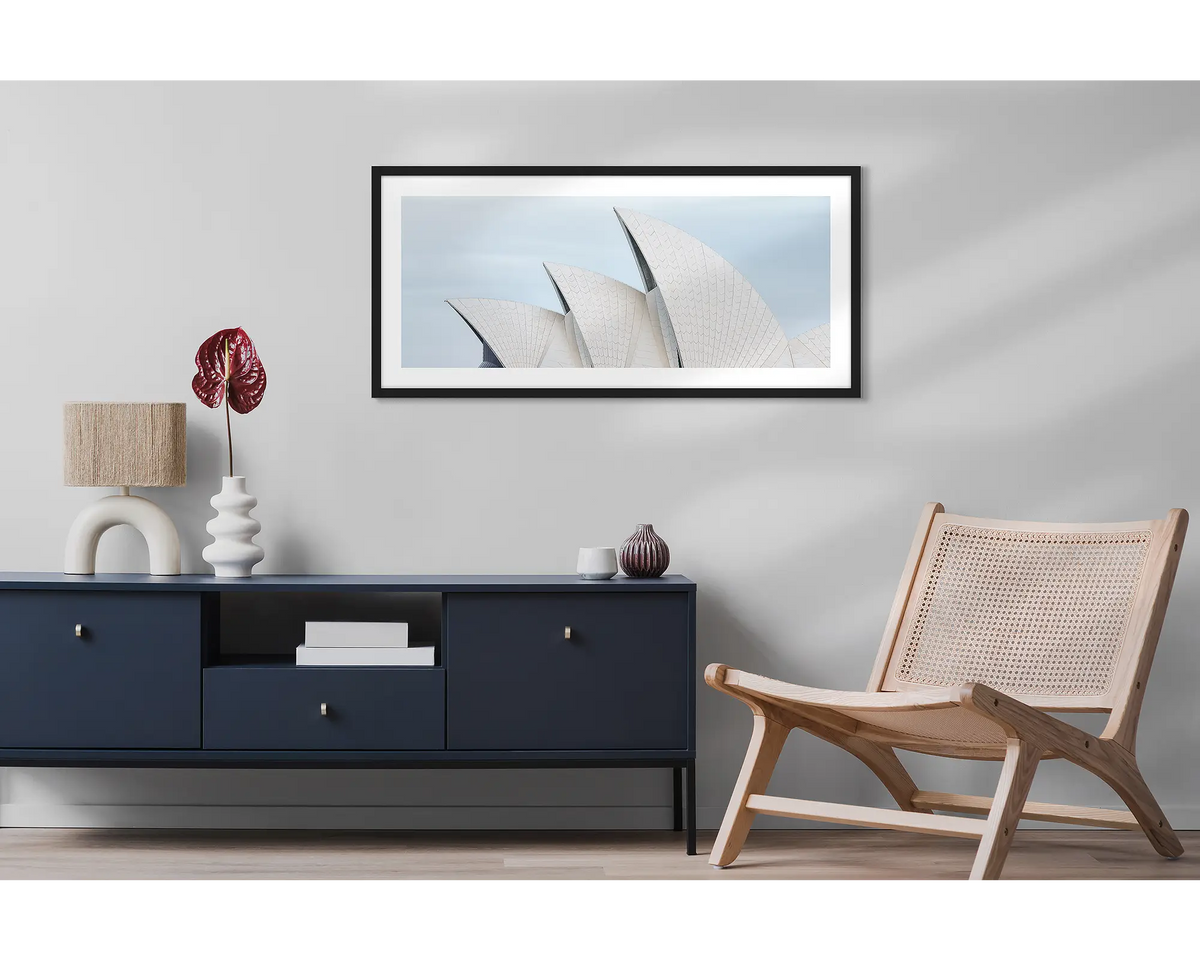Tile Geometry. Wall art print featuring sails of the Sydney Opera House, with a black frame, hung above a side table and chair. 
