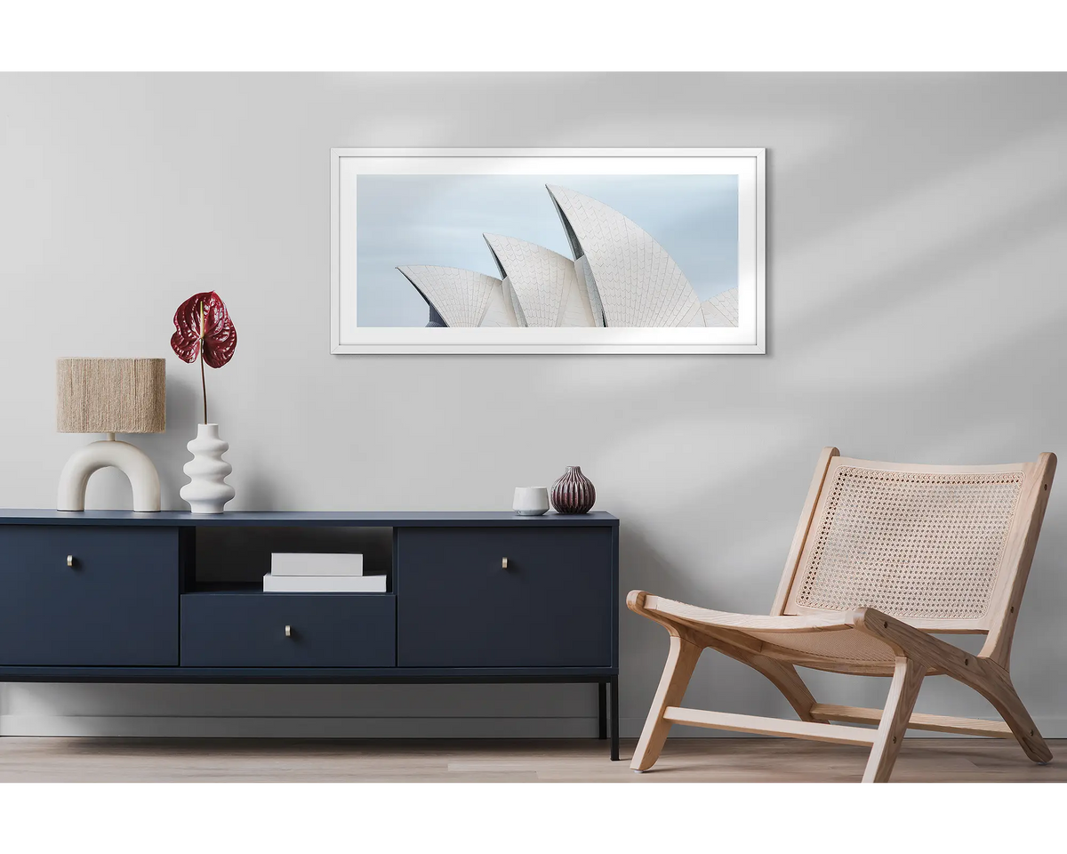Tile Geometry. Wall art print featuring sails of the Sydney Opera House, with a white frame, hung above a side table and chair. 