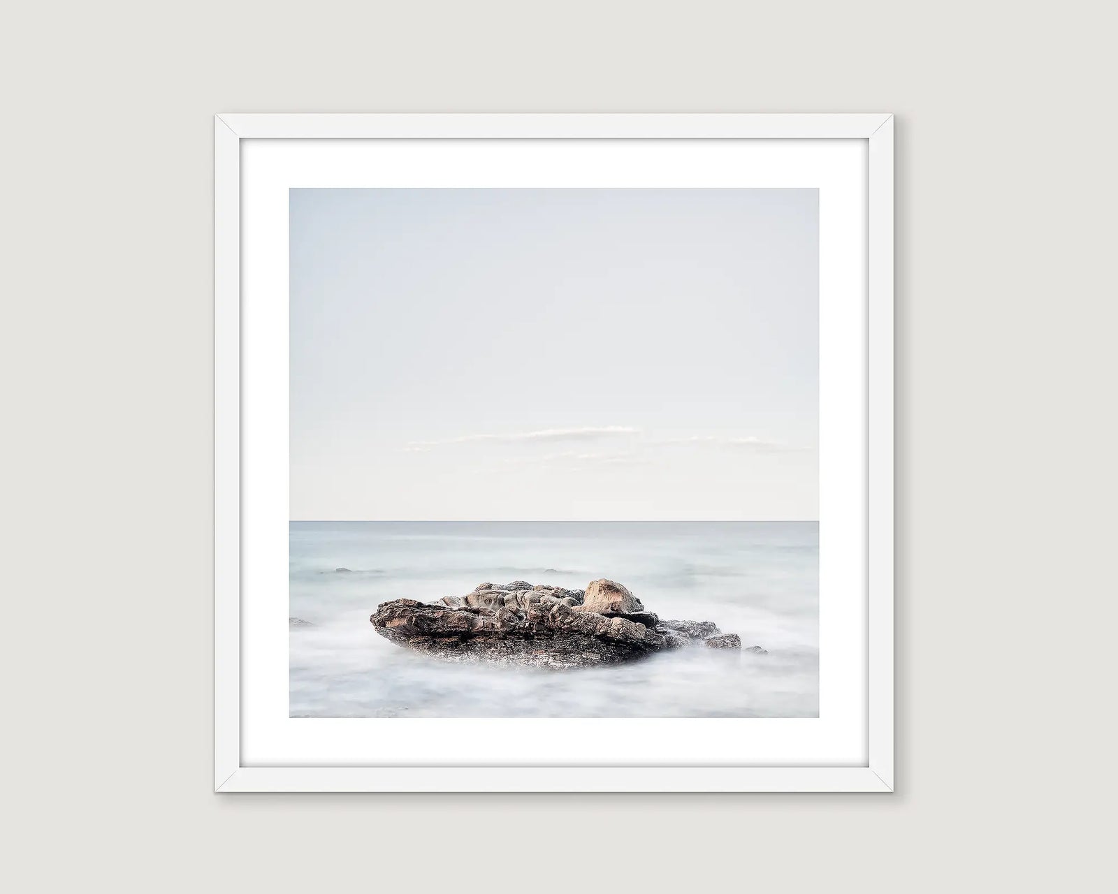 Framed photograph of a rock in the ocean with a white frame.