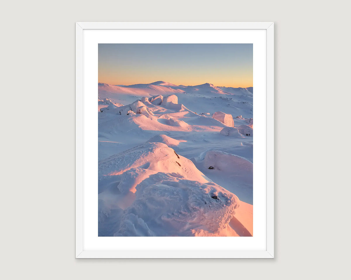 Framed photograph of a snowy landscape with a pink and blue gradient sky.