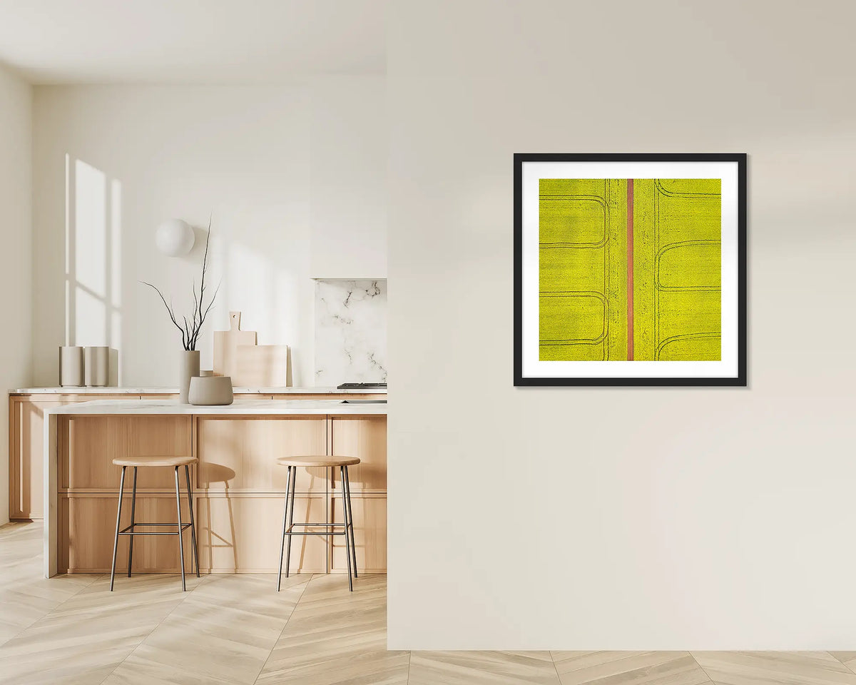 Tracks. Framed wall art print of Canola fields viewed from above, with a black frame, hung on a kitchen wall. 