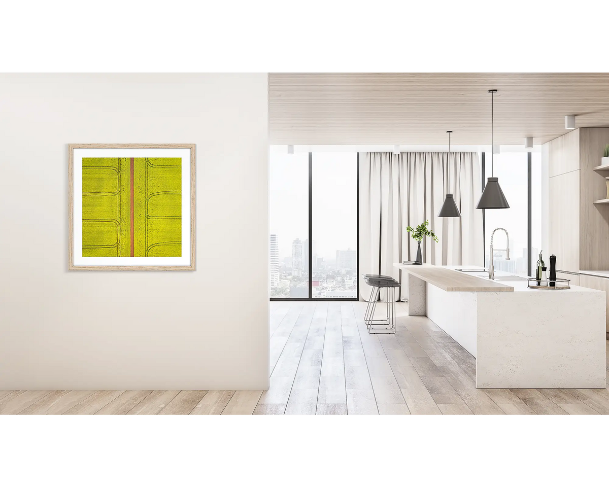 Tracks. Framed wall art print of Canola fields viewed from above, with a timber frame, hung on a hallway wall. 