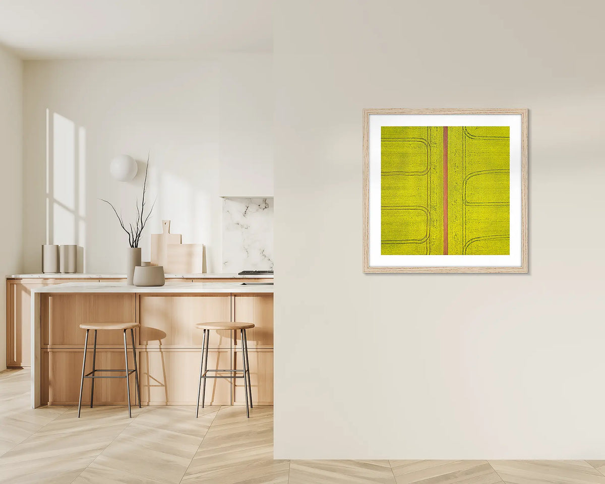 Tracks. Framed wall art print of Canola fields viewed from above, with a timber frame, hung on a kitchen wall. 