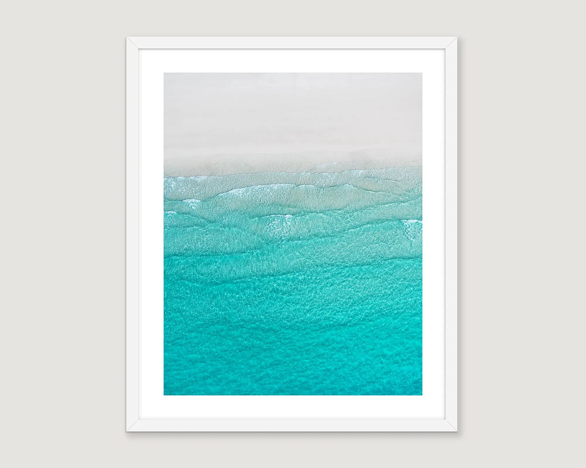 Framed abstract artwork of a turquoise ocean wave on white sand.