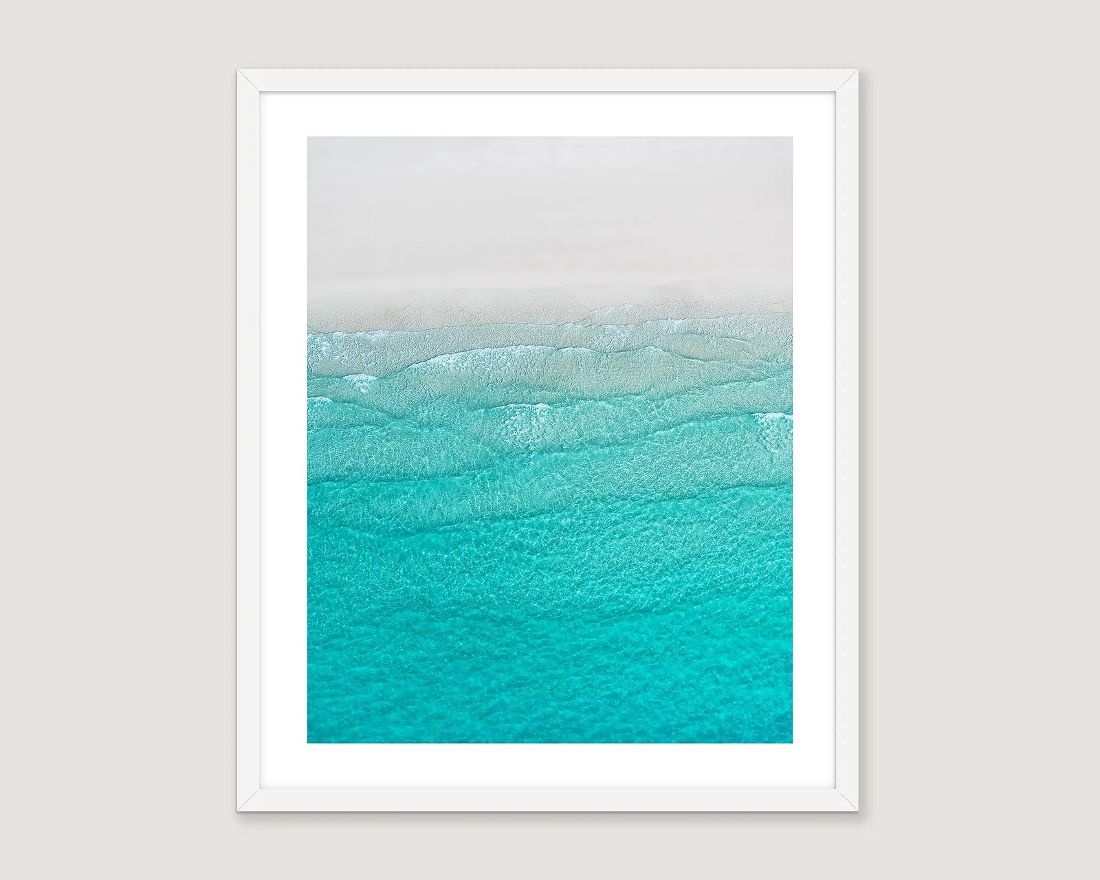 Framed abstract artwork of a turquoise ocean wave on white sand.