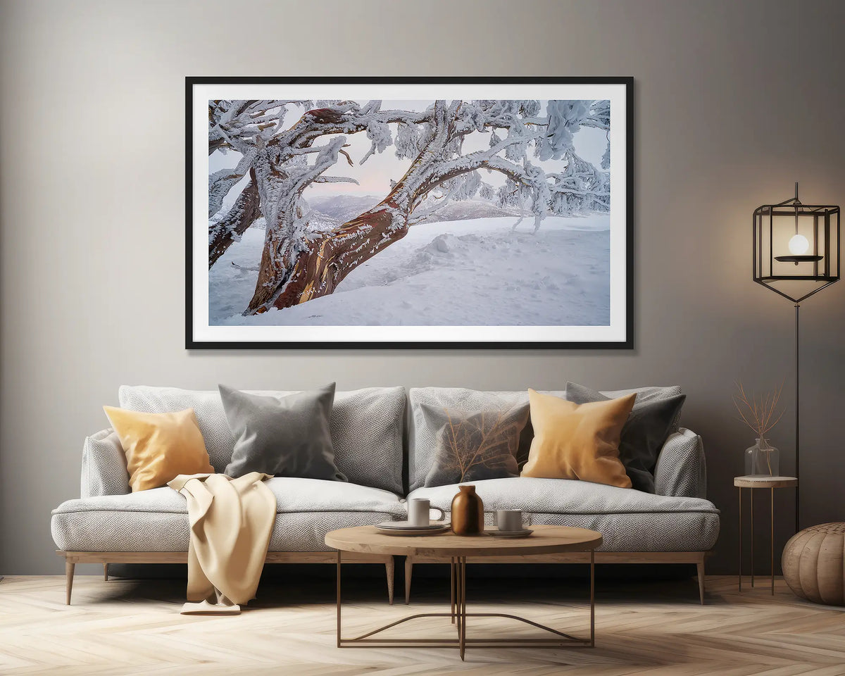 Tree Line. Wall art print of a snow gum in snow with ice at sunset, framed in a black frame and hung above a lounge room couch. 