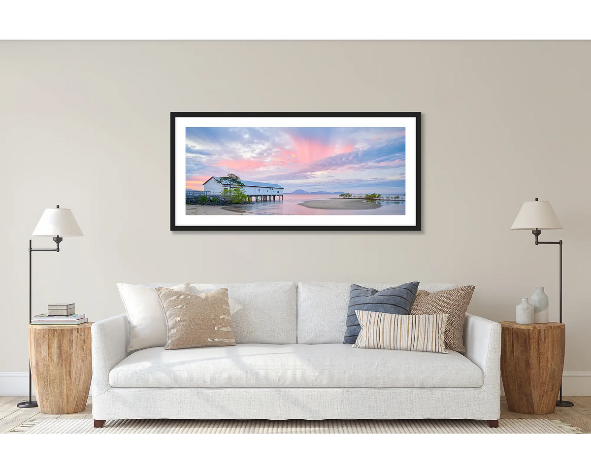 Twilight Blush. Wall art print of a pink sunset over Port Douglas, framed in a black frame, and hung above a couch.