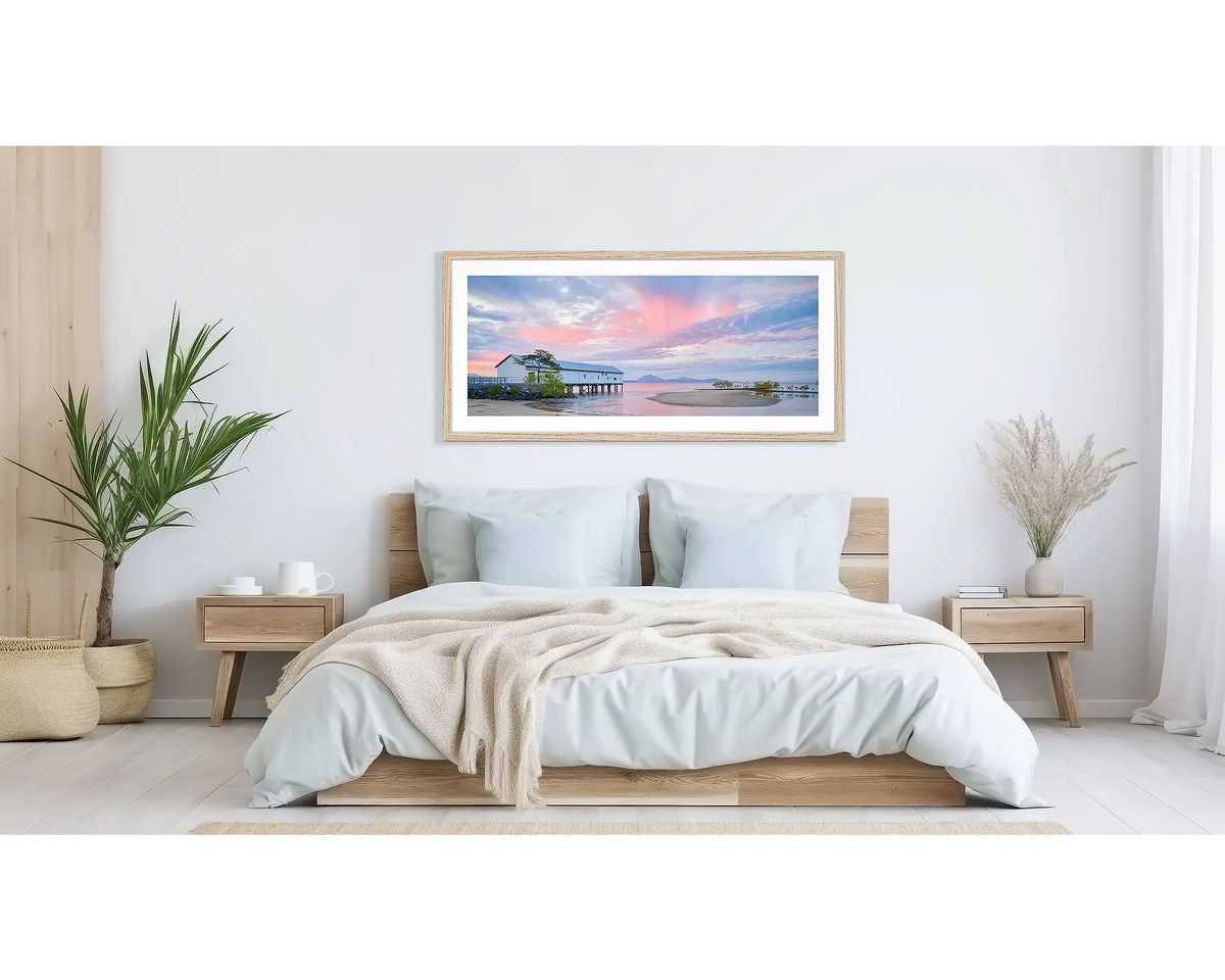 Twilight Blush. Wall art print of a pink sunset over Port Douglas, framed in a timber frame and hung above a bed. 