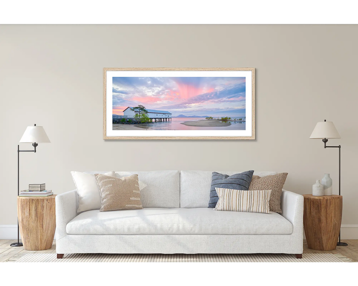 Twilight Blush. Wall art print of a pink sunset over Port Douglas, framed in a timber frame, and hung above a couch.
