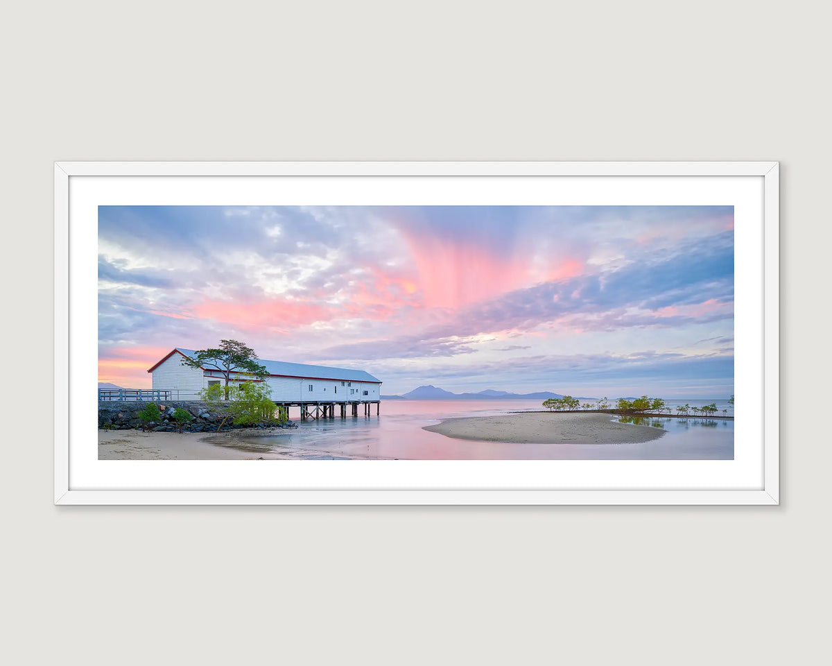 Framed photograph of a coastal scene at Sugar Wharf Port Douglas with a building and trees on a beach at sunset.