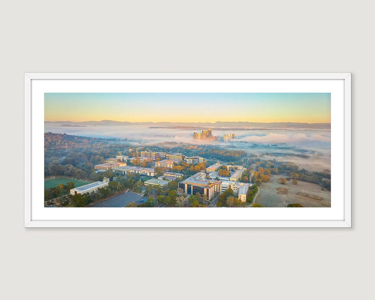 Framed photograph of a cityscape in fog with mountains at sunrise.