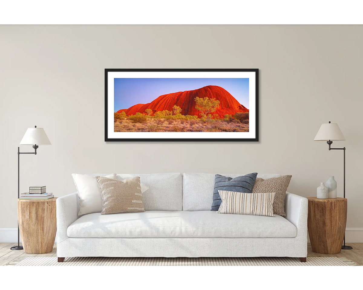 Uluru Awakening. Wall art print of a sunrise at Uluru, framed in a black frame and hung above a couch. 