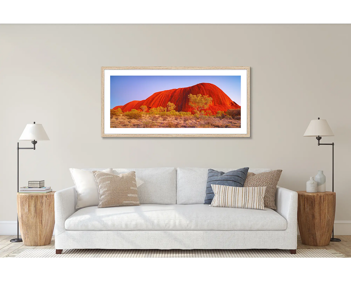 Uluru Awakening. Wall art print of a sunrise at Uluru, framed in a timber frame and hung above a couch. 